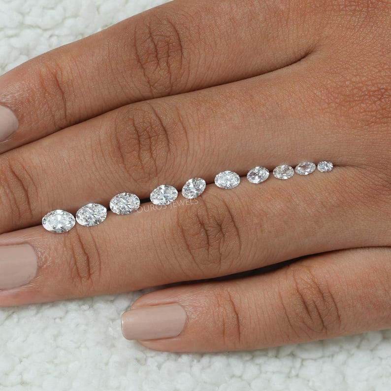 May include: A row of oval-shaped diamonds of varying sizes, arranged from smallest to largest, on a person's hand.