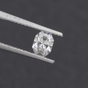 May include: A faceted, oval-cut diamond held by silver tweezers against a dark gray background. The diamond sparkles with internal reflections, showcasing its clarity and brilliance. The gem is a central focus, highlighting its cut and shape.