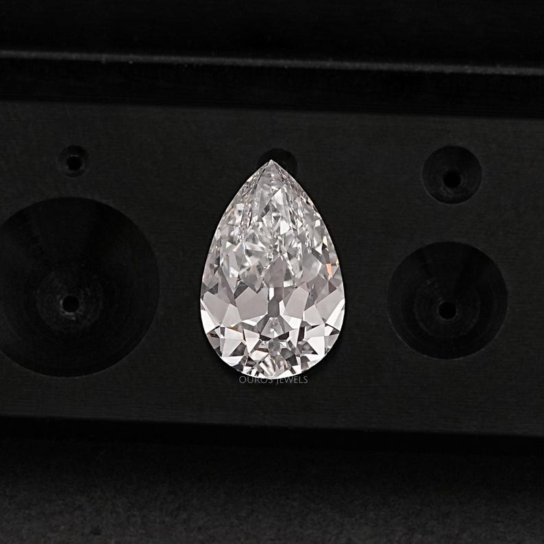May include: A pear-shaped diamond gemstone in a black velvet box. The diamond is clear and has a brilliant cut.
