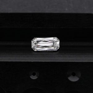 May include: A clear, rectangular emerald cut diamond gemstone on a black background. The diamond has a brilliant, faceted cut.