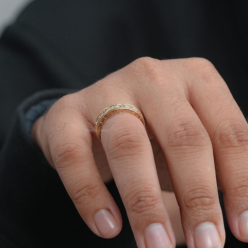 Puede incluir: Un anillo dorado con detalles intrincados y peque&ntilde;os acentos brillantes. El anillo se lleva en un dedo, mostrando su dise&ntilde;o ornamentado. La superficie del anillo tiene una apariencia texturizada, lo que aumenta su atractivo visual. El anillo probablemente est&aacute; hecho de un metal precioso.