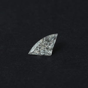 Puede incluir: Un diamante suelto, incoloro y de talla trillion, con forma triangular, esquinas afiladas y m&uacute;ltiples facetas que crean una superficie brillante y reflectante. La piedra muestra una claridad interna n&iacute;tida y refracci&oacute;n.