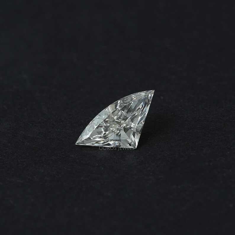 Puede incluir: Un diamante suelto, incoloro y de talla trillion, con forma triangular, esquinas afiladas y m&uacute;ltiples facetas que crean una superficie brillante y reflectante. La piedra muestra una claridad interna n&iacute;tida y refracci&oacute;n.