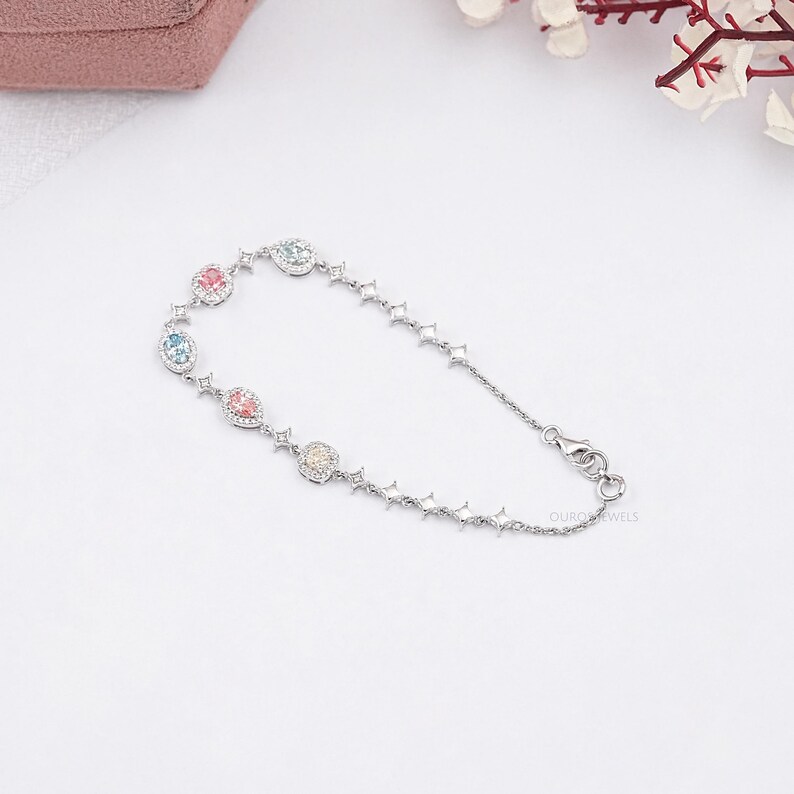 Puede incluir: Un brazalete de plata con una cadena delicada y peque&ntilde;as piedras preciosas de colores engastadas en un marco de plata. El brazalete tiene un dise&ntilde;o en forma de estrella y un cierre de broche. "OURJOY JEWELS" est&aacute; impreso en el broche.