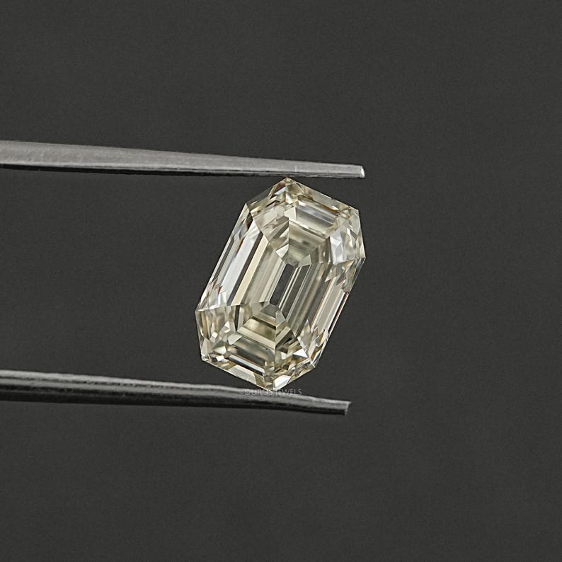May include: A light yellow emerald cut diamond gemstone held by tweezers against a dark grey background.