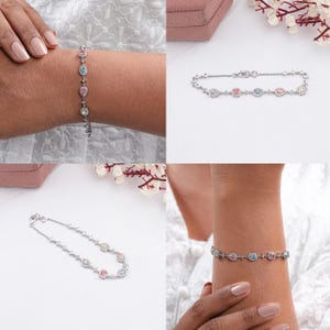Puede incluir: Un brazalete de plata con una cadena delicada y piedras ovaladas en tonos rosa, azul y blanco.