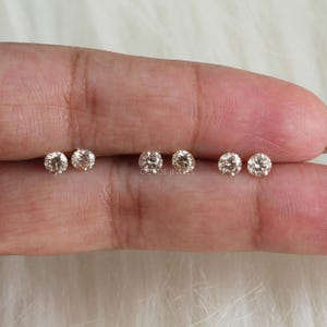 May include: Six round, clear, gemstone earrings in various sizes. The earrings are displayed on a hand.