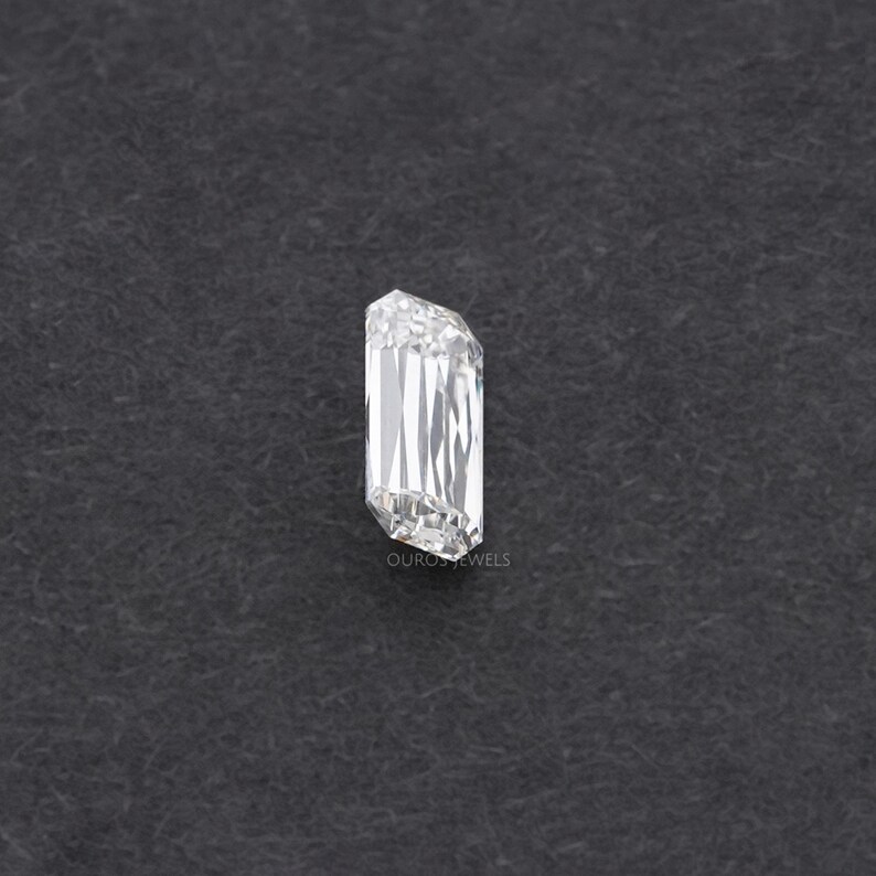 May include: A clear, rectangular emerald cut diamond gemstone on a dark gray background.