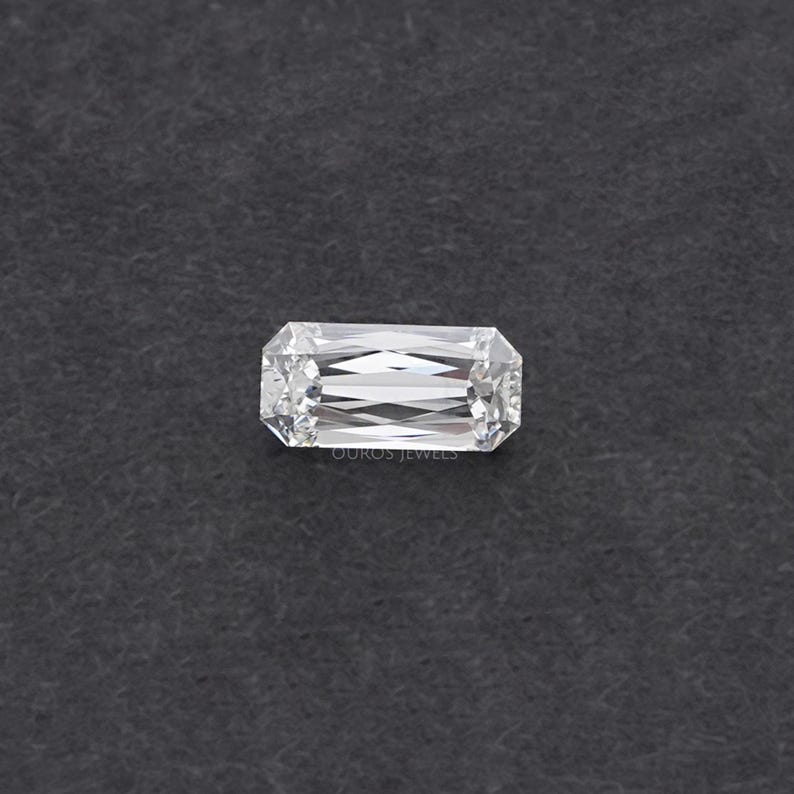 May include: A clear, rectangular emerald cut diamond gemstone with facets.