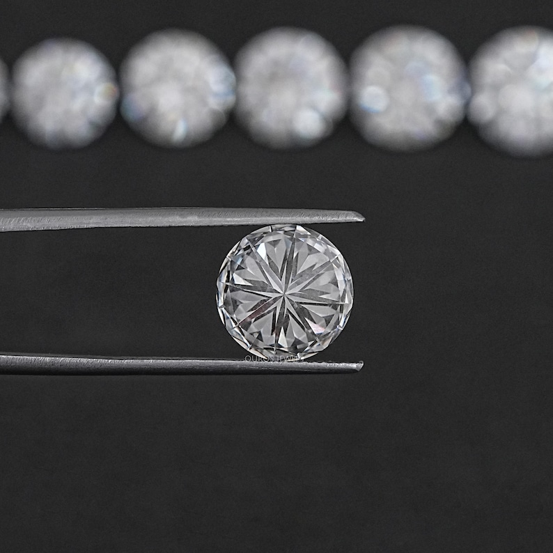 May include: A clear round diamond gemstone held by tweezers against a black background. The diamond has a star-shaped pattern.