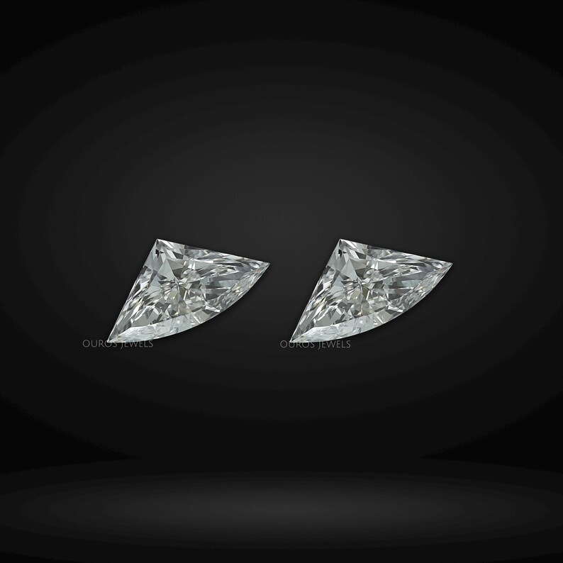 Puede incluir: Dos diamantes sueltos de talla escudo con una superficie facetada brillante y un aspecto claro e incoloro. Cada piedra presenta el texto Ouros Jewels impreso en peque&ntilde;as letras blancas cerca del borde inferior sobre un fondo oscuro.