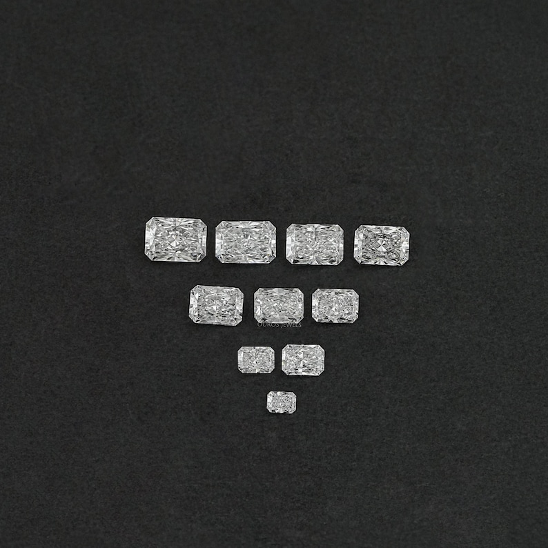 Puede incluir: Una colecci&oacute;n de piedras preciosas rectangulares, facetadas y transparentes, dispuestas en forma de tri&aacute;ngulo sobre un fondo negro.