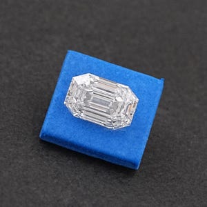 May include: A clear emerald cut diamond on a blue velvet cushion.
