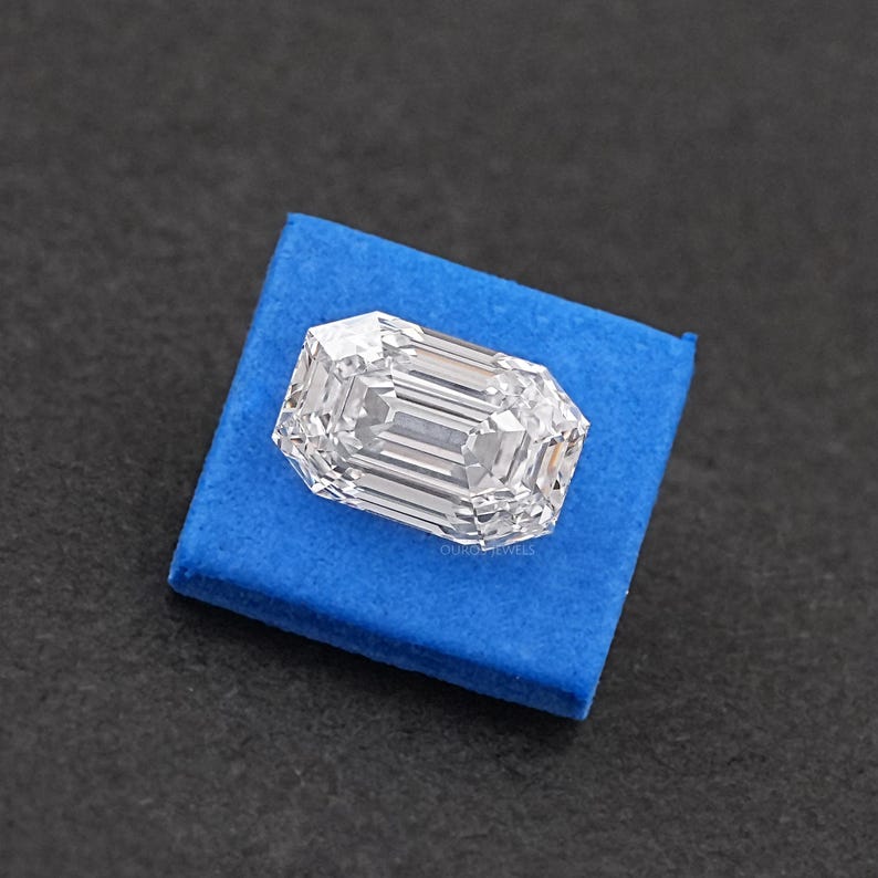 May include: A clear emerald cut diamond on a blue velvet cushion.