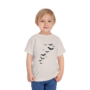 May include: A light heather gray short-sleeved t-shirt featuring a graphic print of a flock of small black bats flying in an upward diagonal pattern across the center of the chest. The shirt has a crew neckline and a standard fit.