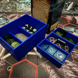 May include: Two blue plastic storage boxes with dividers. The larger box contains various game pieces, including tokens and dice. The smaller box contains smaller game pieces.