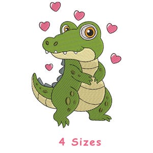 May include: An embroidery design featuring a cartoon green crocodile with large eyes, a light-colored belly, and dark green spots on its back. The crocodile is surrounded by five small pink hearts. The text 4 Sizes is printed in pink below.