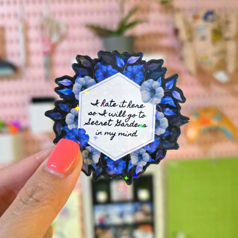 May include: A blue and white floral sticker with a hexagonal white background and the text "I hate it here so I will go to secret gardens in my mind".