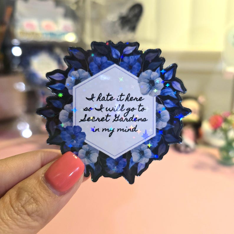 May include: A blue and white floral sticker with a hexagonal frame and the text "I hate it here so I will go to secret gardens in my mind".