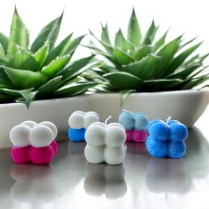 May include: Five small, round, decorative candles in various colours. The candles are shaped like a cluster of four spheres. The colours are white, pink, blue, and light blue.