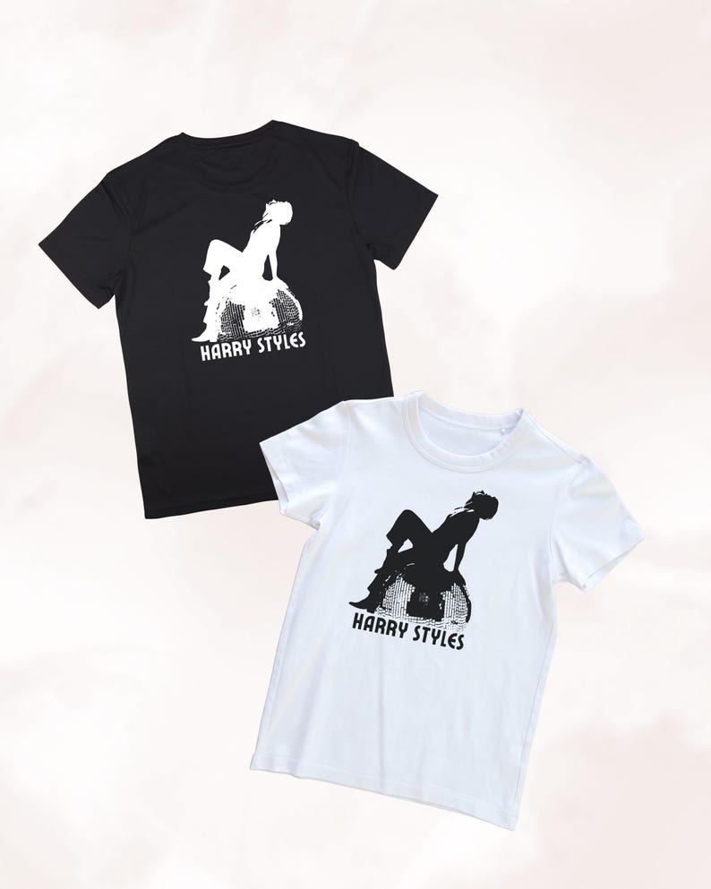May include: A black t-shirt and a white t-shirt, each featuring a graphic print of a person sitting on a disco ball with the text HARRY STYLES printed underneath in a bold, sans-serif font. The black shirt has a white graphic, and the white shirt has a black graphic.
