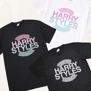 May include: Three short-sleeve t-shirts, one white and two black. Each shirt features a graphic print with the text "HARRY STYLES" in large letters, surrounded by the word "TOGETHER" in a circular outline. The print colors vary by shirt.