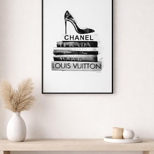 Puede incluir: Impresi&oacute;n enmarcada en blanco y negro con un zapato de tac&oacute;n alto sobre una pila de libros. Los libros muestran los nombres Chanel, Prada, Tiffany & Co., Dior, Vogue y Louis Vuitton. Una impresi&oacute;n art&iacute;stica minimalista de moda.