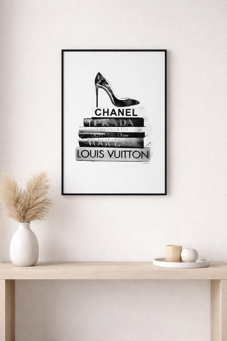 Puede incluir: Impresi&oacute;n enmarcada en blanco y negro con un zapato de tac&oacute;n alto sobre una pila de libros. Los libros muestran los nombres Chanel, Prada, Tiffany & Co., Dior, Vogue y Louis Vuitton. Una impresi&oacute;n art&iacute;stica minimalista de moda.