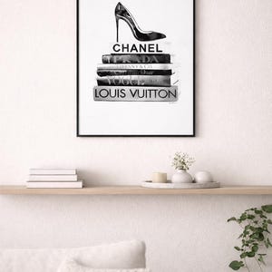 Puede incluir: Impresi&oacute;n en blanco y negro enmarcada que representa un zapato de tac&oacute;n alto sobre una pila de libros de moda. Los libros incluyen t&iacute;tulos como "Chanel" y "Louis Vuitton". La impresi&oacute;n se muestra encima de una estanter&iacute;a con objetos decorativos.