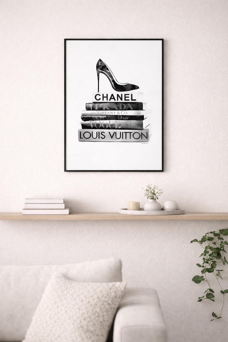 Puede incluir: Impresi&oacute;n en blanco y negro enmarcada que representa un zapato de tac&oacute;n alto sobre una pila de libros de moda. Los libros incluyen t&iacute;tulos como "Chanel" y "Louis Vuitton". La impresi&oacute;n se muestra encima de una estanter&iacute;a con objetos decorativos.