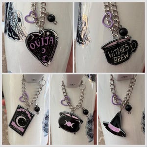 May include: Four white mugs with black and purple charms attached to silver chains. The charms include a Ouija board, a cauldron, a witch's hat, and a cup that says "Witches Brew".