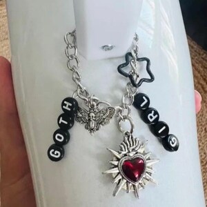 May include: A silver charm bracelet with black beads spelling "GOTH GIRL" and charms including a silver moth, a star, and a silver heart with a red gem.
