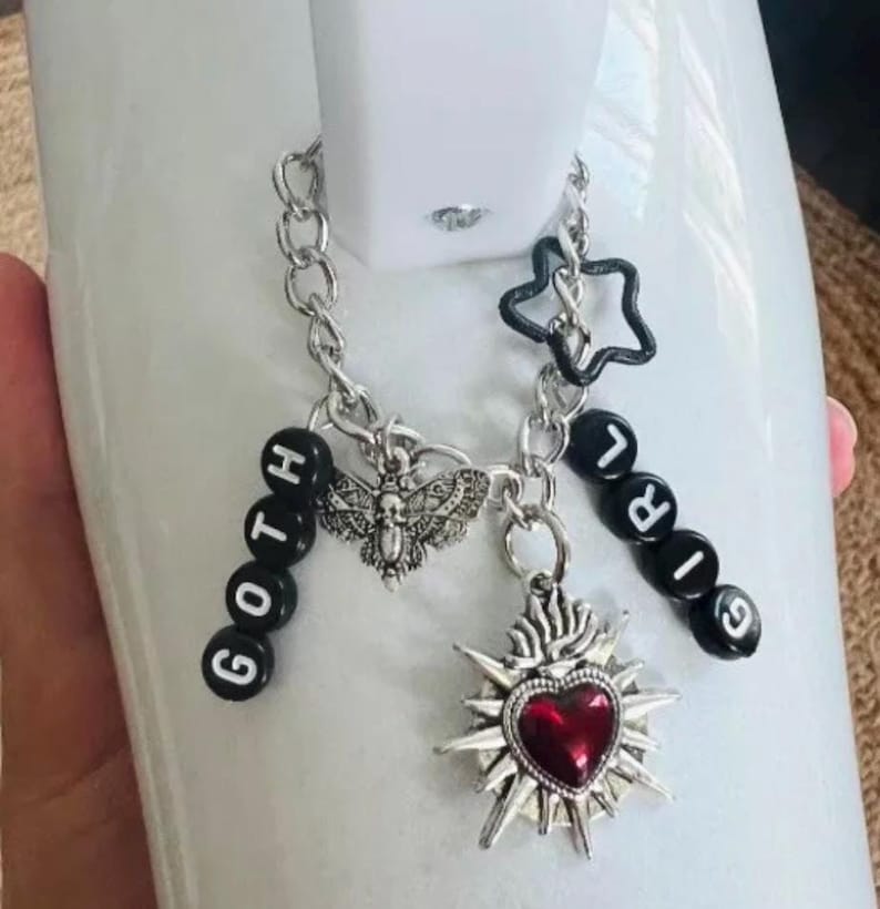 May include: A silver charm bracelet with black beads spelling "GOTH GIRL" and charms including a silver moth, a star, and a silver heart with a red gem.