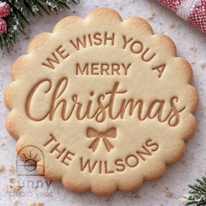 May include: A round, scalloped-edge sugar cookie with an embossed design. The text reads WE WISH YOU A MERRY Christmas THE WILSONS, featuring a small bow icon centered between the last two lines of text in a light brown, baked finish.