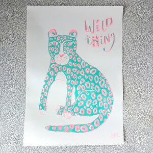 Op de afbeelding: Een turquoise en roze luipaardprint illustratie met de tekst "Wild Thing" in roze en turquoise letters.
