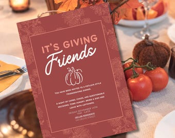 May include: A maroon Friendsgiving invitation with white script text and a pumpkin illustration. The invitation includes event details: date, time, and location. The invitation is on a table with tomatoes and a decorative pumpkin.
