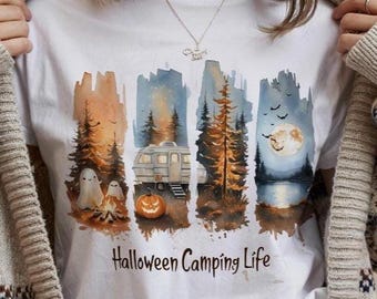 Puede incluir: Camiseta blanca con un diseño de acuarela de una escena de camping con una caravana, árboles, una fogata, fantasmas y una calabaza. El texto "Halloween Camping Life" está impreso debajo. El diseño tiene tonos naranja, azul y marrón.