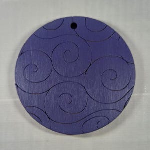 Può includere: Un ornamento rotondo in legno di colore viola con un motivo a spirale intagliato sulla superficie. L'ornamento ha un foro nella parte superiore per appenderlo.