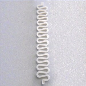 May include: A white, wavy, plastic component with a repeating, serpentine design. The component is long and narrow, with a series of rounded curves. The object is likely a part of a larger product or mechanism.