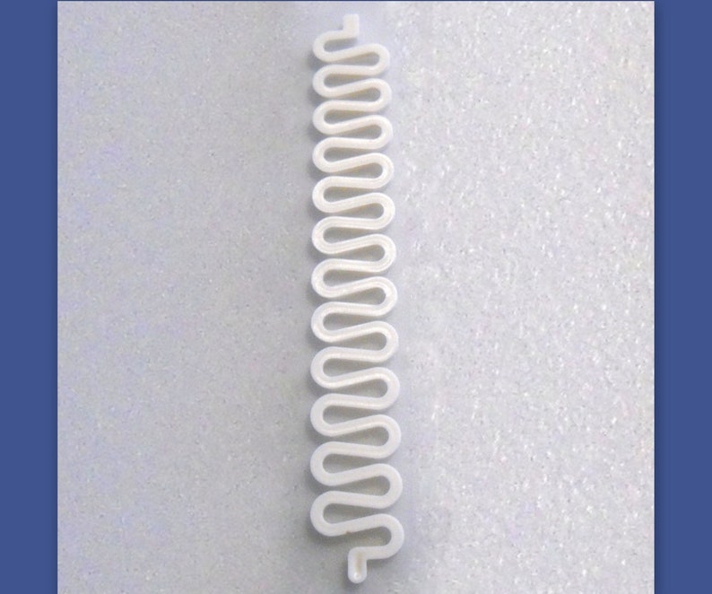 May include: A white, wavy, plastic component with a repeating, serpentine design. The component is long and narrow, with a series of rounded curves. The object is likely a part of a larger product or mechanism.