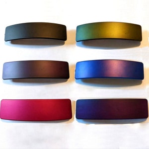 May include: Six hair clips in different colors. The clips are all the same size and shape, and they are made of a smooth, shiny material. The colors are black, green, purple, blue, red, and dark purple.