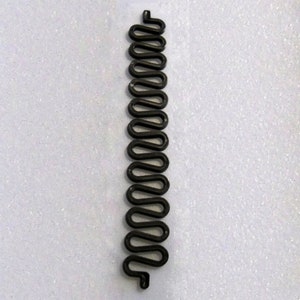 May include: A black, wavy metal object, resembling a stylized snake or spring, is displayed against a white background. The object has a repeating, curved design, and is likely a decorative or functional item.