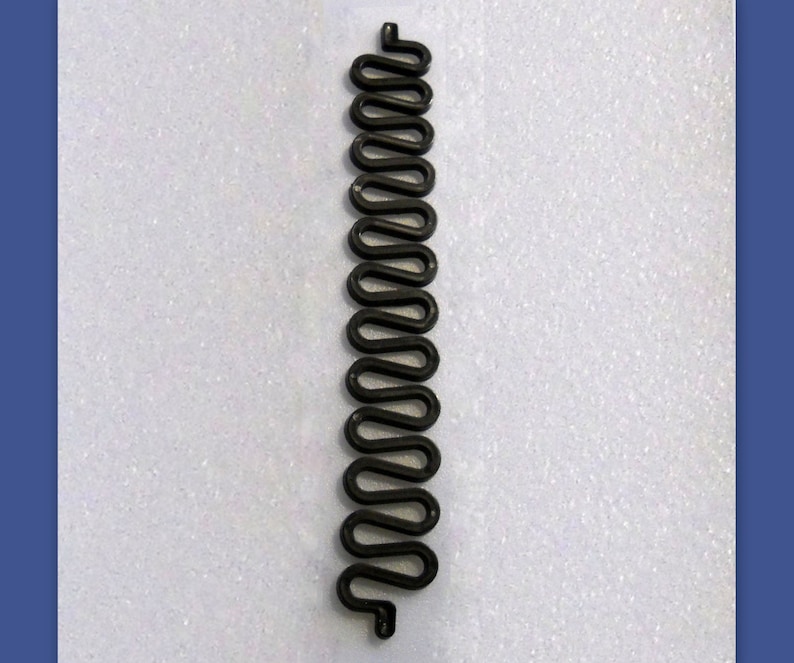 May include: A black, wavy metal object, resembling a stylized snake or spring, is displayed against a white background. The object has a repeating, curved design, and is likely a decorative or functional item.