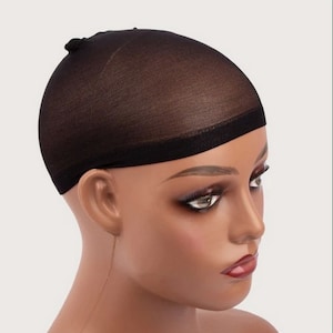 May include: A black wig cap made of a fine mesh material. The cap is designed to cover the head and is worn under wigs or hairpieces. The cap is shown on a mannequin head with a neutral background.