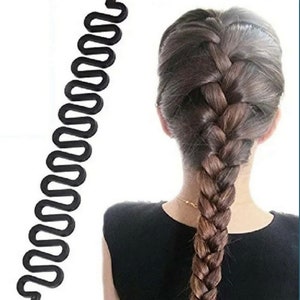 May include: A black hair braiding tool with a wavy design is shown next to a person's braided hair. The hair is a mix of brown and blonde shades. The tool is designed to help create intricate braided hairstyles.