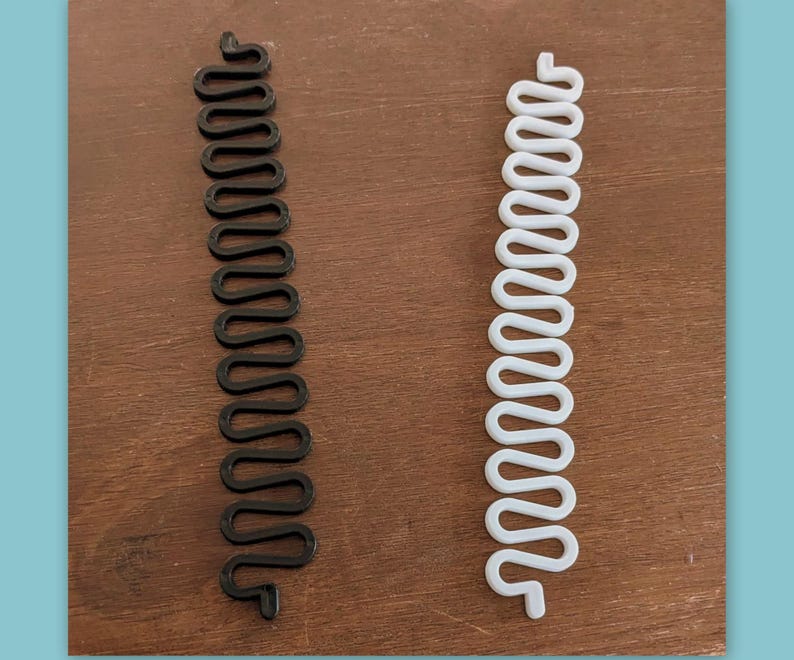 May include: Two hair accessories are displayed. One is black, the other is white. Both are made of a flexible material and have a wavy, zig-zag design. These hair accessories are designed to be woven into the hair to create a unique style.