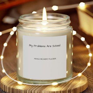 May include: A white candle in a glass jar with a label that reads "My Problems Are Solved, Peace in Every Flicker". The candle is lit and surrounded by white fairy lights.