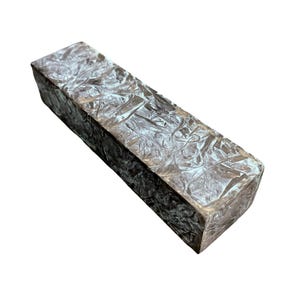 Puede incluir: Un bloque rectangular de resina marrón oscuro con un patrón de remolino marmoleado en tonos de blanco y gris.