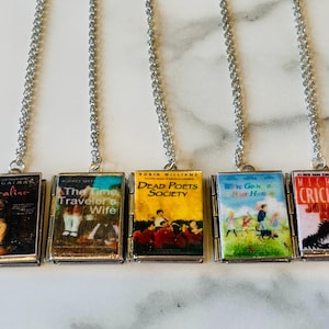 May include: Five silver chain necklaces, each with a miniature book pendant. The book covers feature titles like "Coraline" and "The Time Traveler's Wife." The pendants are rectangular with detailed book cover art.