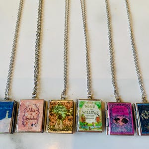 May include: Six silver-toned necklaces each feature a miniature book pendant. The book covers display titles like "The Little Prince," "Alice in Wonderland," and "Mary Poppins." The pendants are rectangular with hinged openings.
